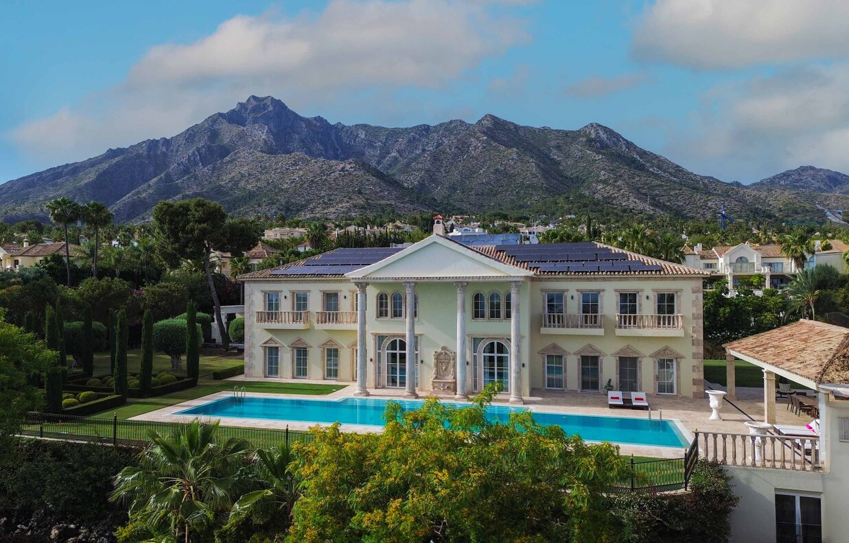 Luxury villa in Marbella featuring expansive glazing, rooftop solar panels, a green roof, and stunning La Concha mountain vistas.