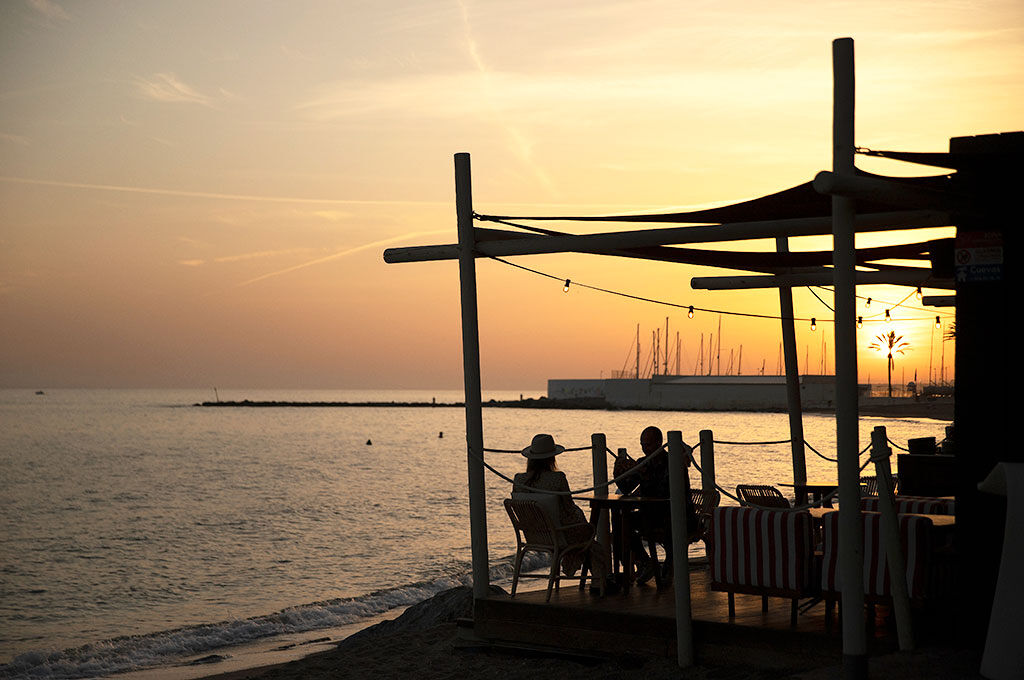 A family gathers on a sun-kissed terrace, savoring delicious food as the Marbella sky glows in warm sunset hues—a perfect evening of laughter, flavors, and togetherness by the Mediterranean.
