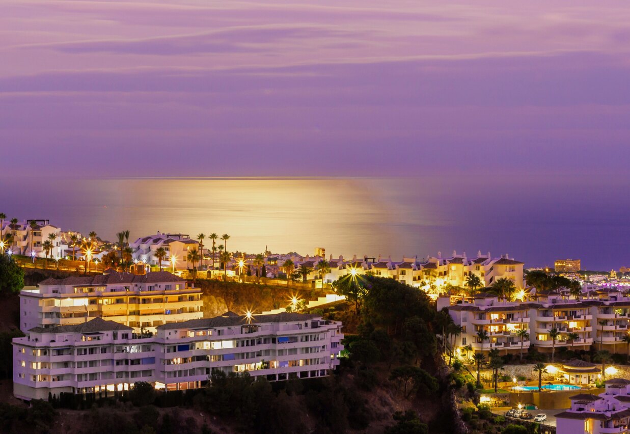 Aerial view of Marbella coastline at dusk with city lights and Mediterranean Sea.