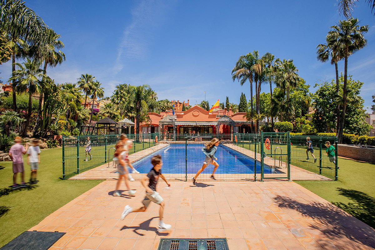 Children playing in a secure international school campus in Marbella with swimming pool and palm trees.