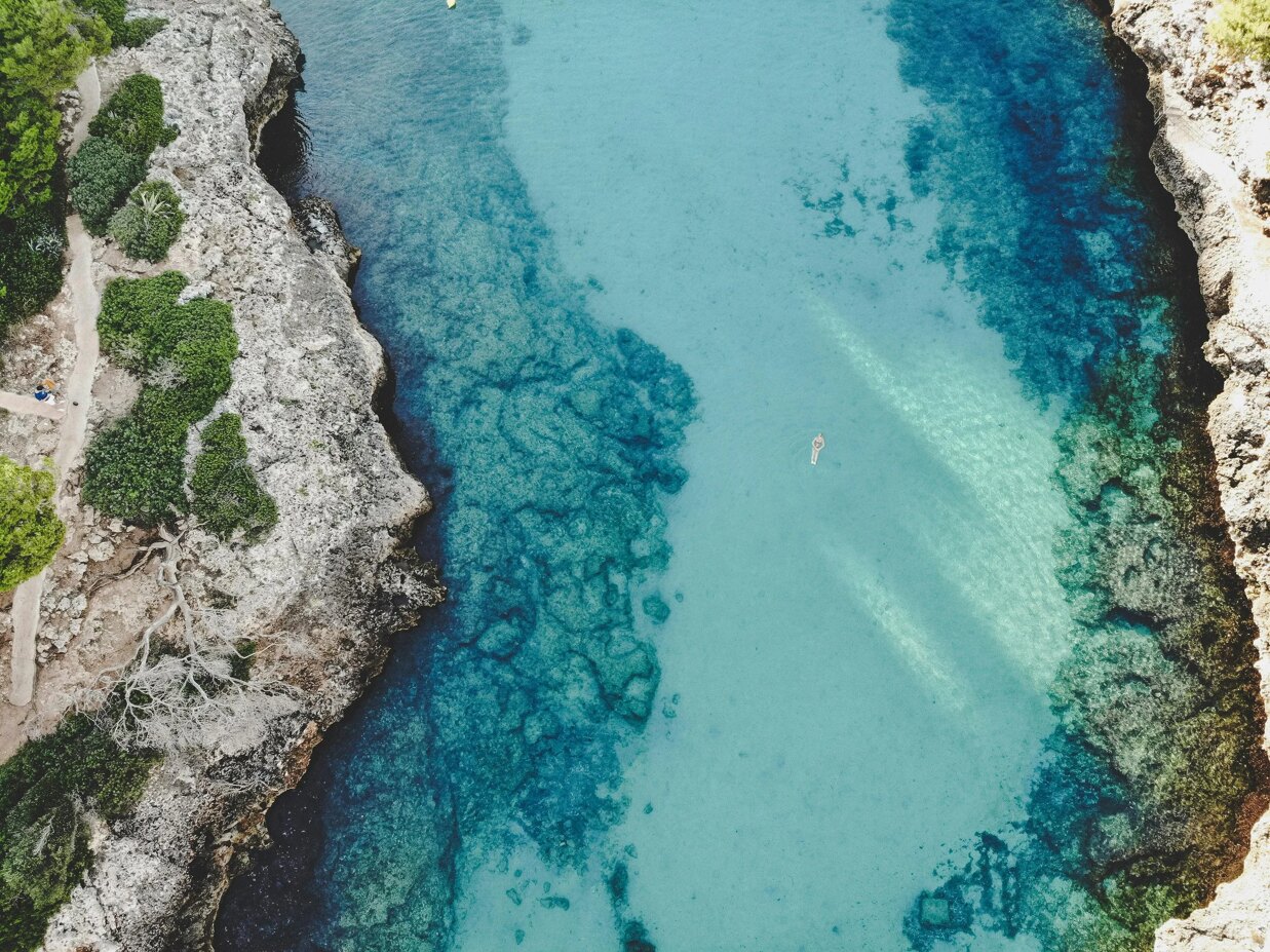 Aerial view of a turquoise cove with clear water and rocky coastline in Mallorca