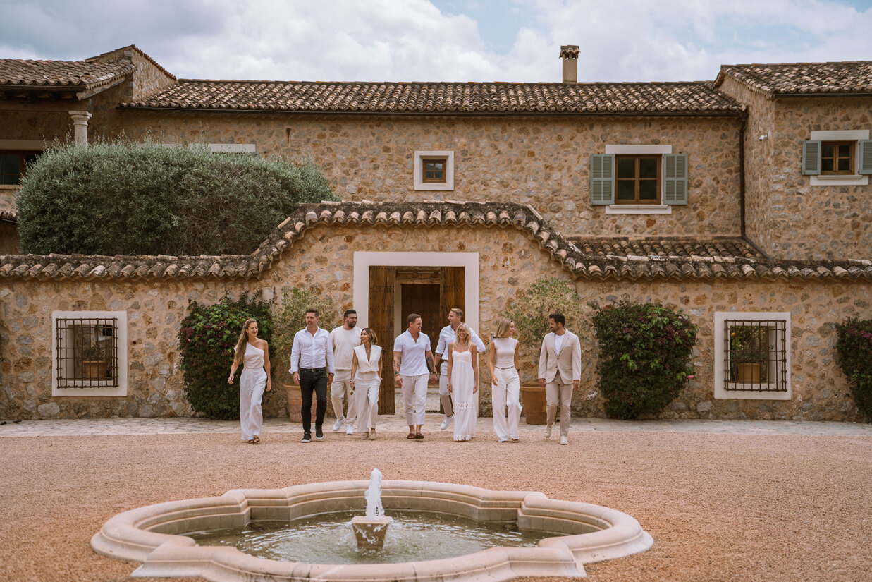 The Homerun Brokers Team standing in front of a stone finca with fountain in a traditional courtyard in Mallorca.