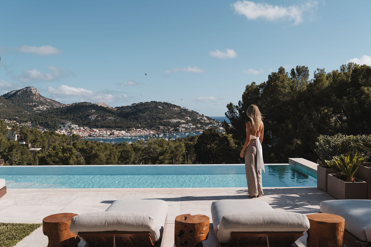 Woman standing by an infinity pool overlooking a bay and hillside in southwest Mallorca