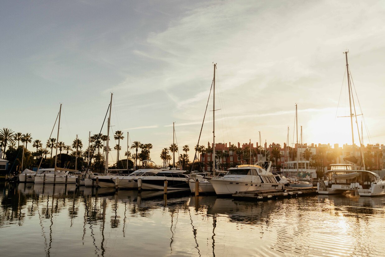 Luxury yachts docked in Sotogrande Marina with calm water reflections and Mediterranean sunset.