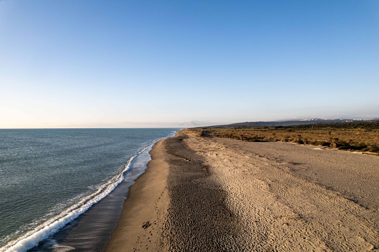 A breathtaking view of Sotogrande’s beach, with crystal-clear blue waters, golden sand, and Gibraltar rising majestically on the horizon under the warm Mediterranean sun.