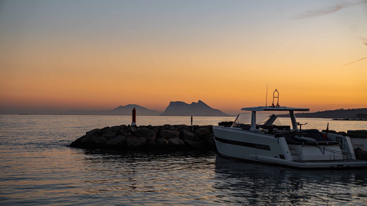 Boat at sunset in Sotogrande with Gibraltar in the background and calm Mediterranean waters.