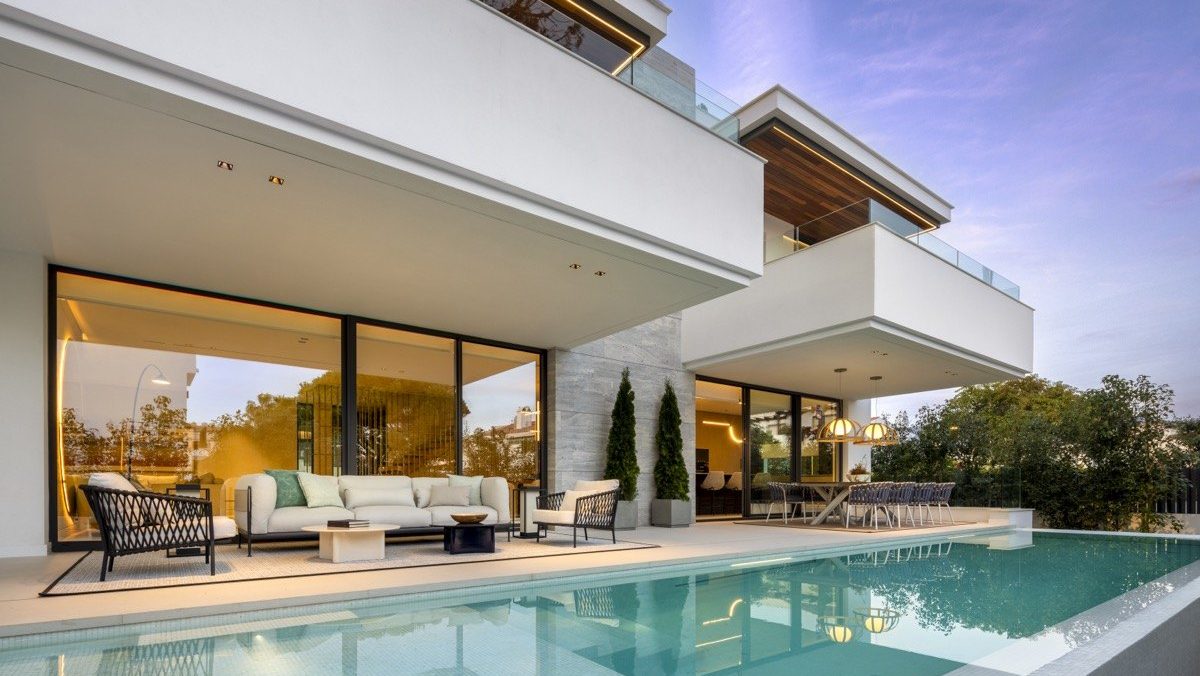 Modern villa with clean lines, large glass doors, and an infinity pool, blending indoor and outdoor living spaces at sunset.