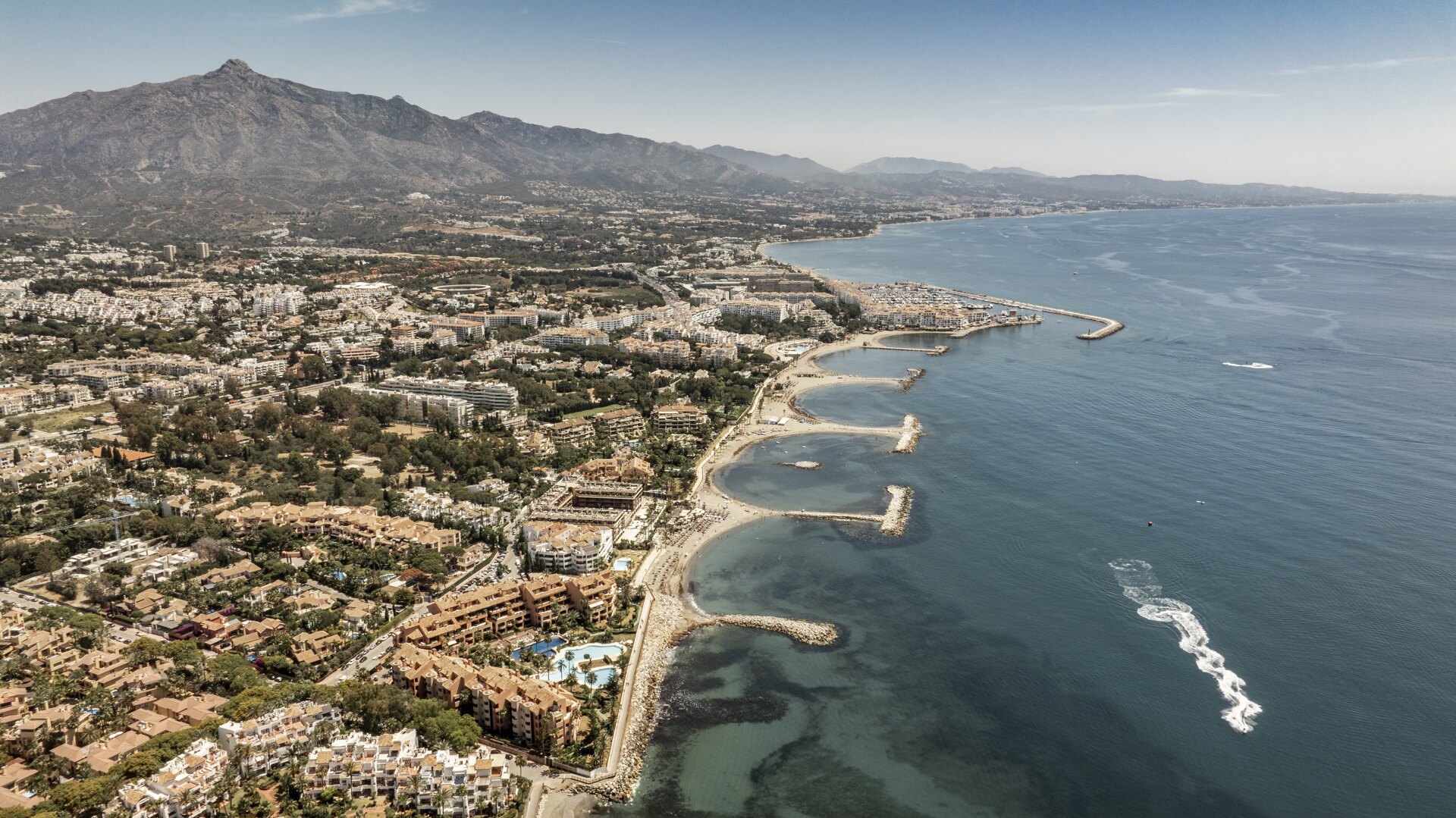 Aerial view of San Pedro Alcántara’s coastline, with breakwaters, sandy beaches, and La Concha mountain in the background.