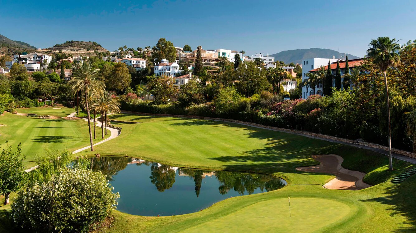 Lush golf course at The Westin La Quinta, surrounded by palm trees, a reflective pond, and Mediterranean-style villas under a clear blue sky.