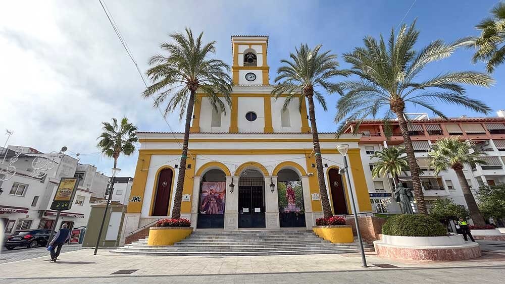 Yellow and white church with a clock tower, arched entrance, and palm trees in San Pedro Alcántara, blending traditional and Andalusian architecture.