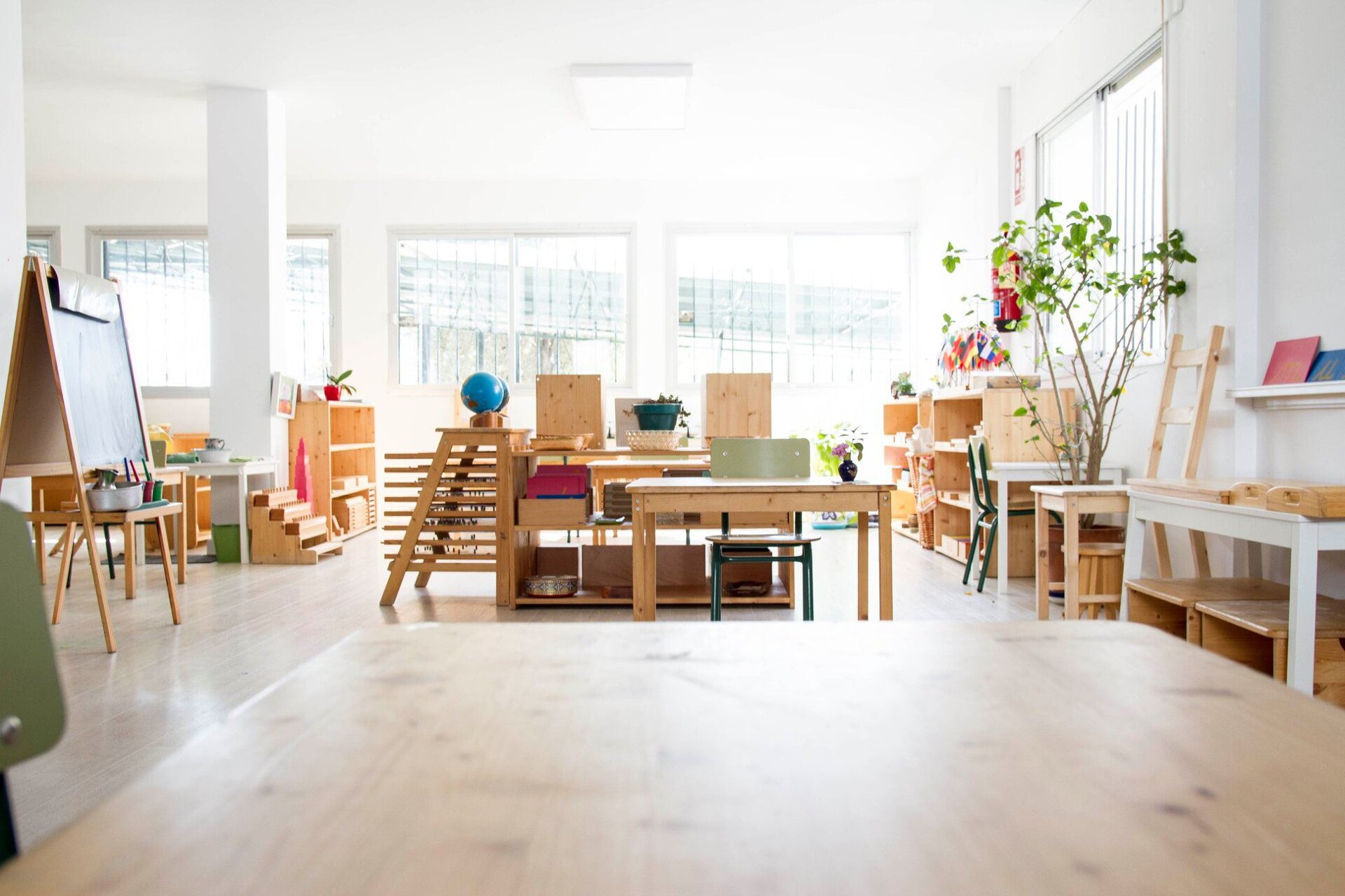 Bright Montessori classroom with natural wooden furniture, learning materials, and plants, creating a warm and engaging environment.