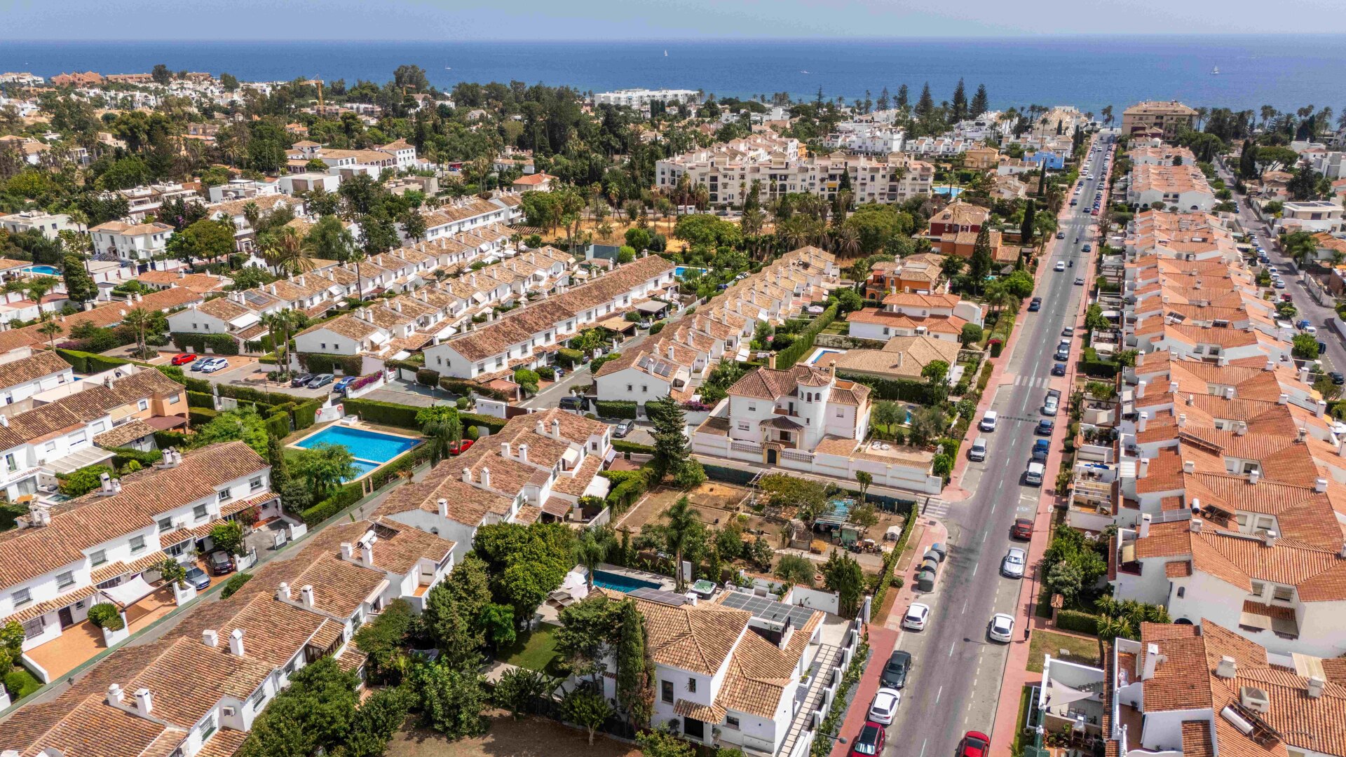 Aerial view of San Pedro Alcántara, showing white Mediterranean-style houses, a tree-lined avenue, and the sea in the background.