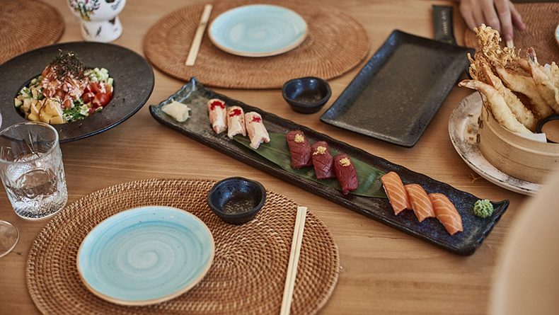 A beautifully set table with sushi, tempura, and fresh dishes on woven placemats, capturing the essence of Japanese cuisine in a coastal setting.