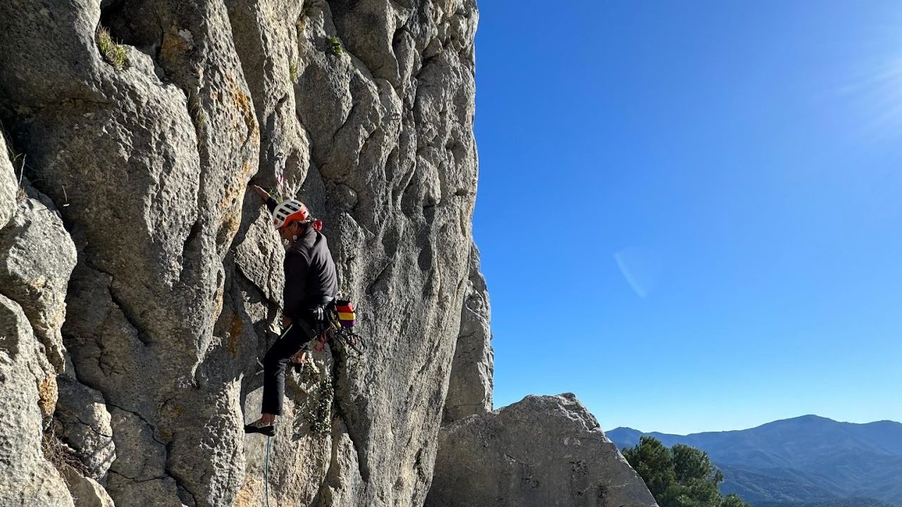 Rock climbing adventure with panoramic mountain views under a clear blue sky.