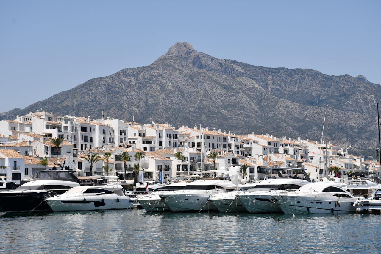 Puerto Banús marina with luxury yachts, white Mediterranean-style buildings, and La Concha mountain in the background.