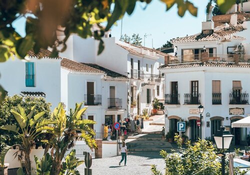 Charming street scene in Frigiliana, a picturesque Andalusian village with whitewashed houses, terracotta rooftops, and lush greenery, bathed in warm Mediterranean sunlight.