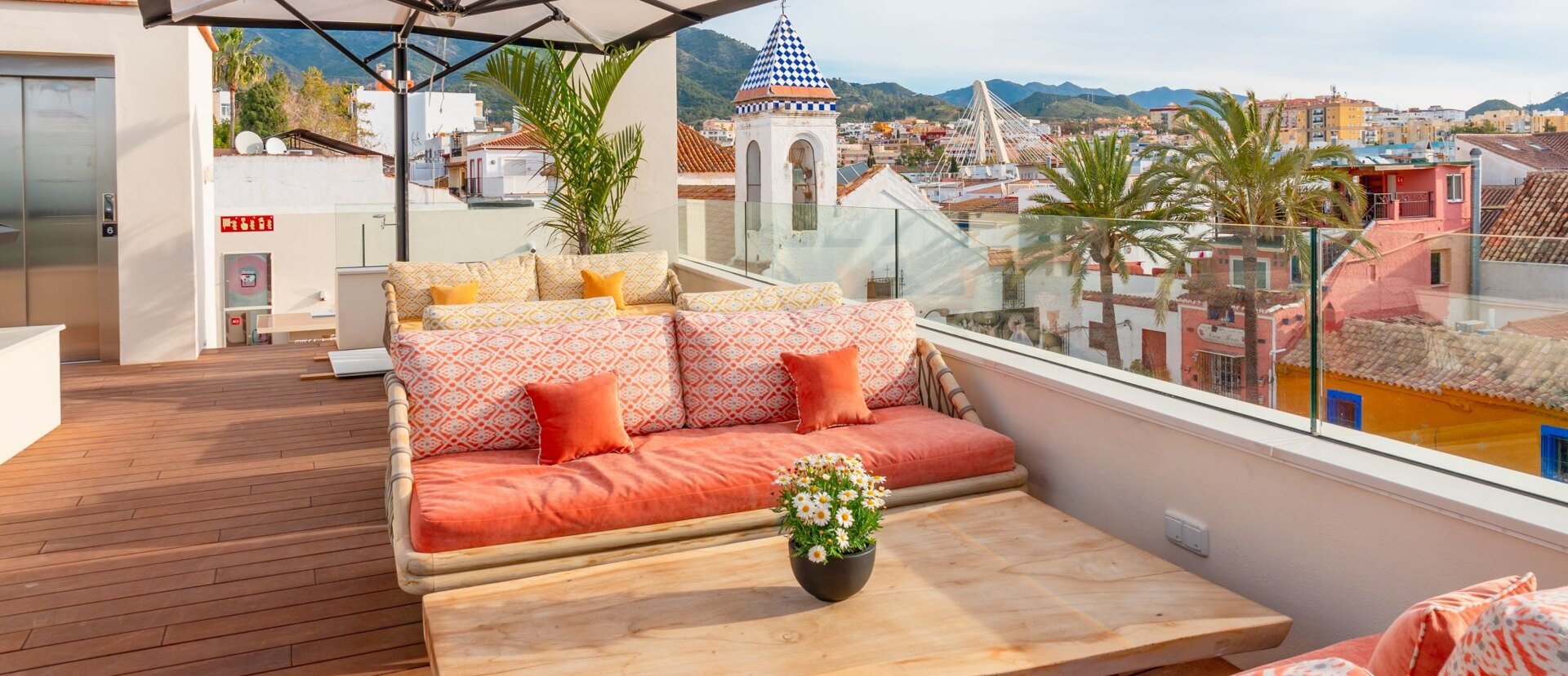 Terrace with colorful sofas and a glass railing overlooking the narrow streets of Marbella's old town.