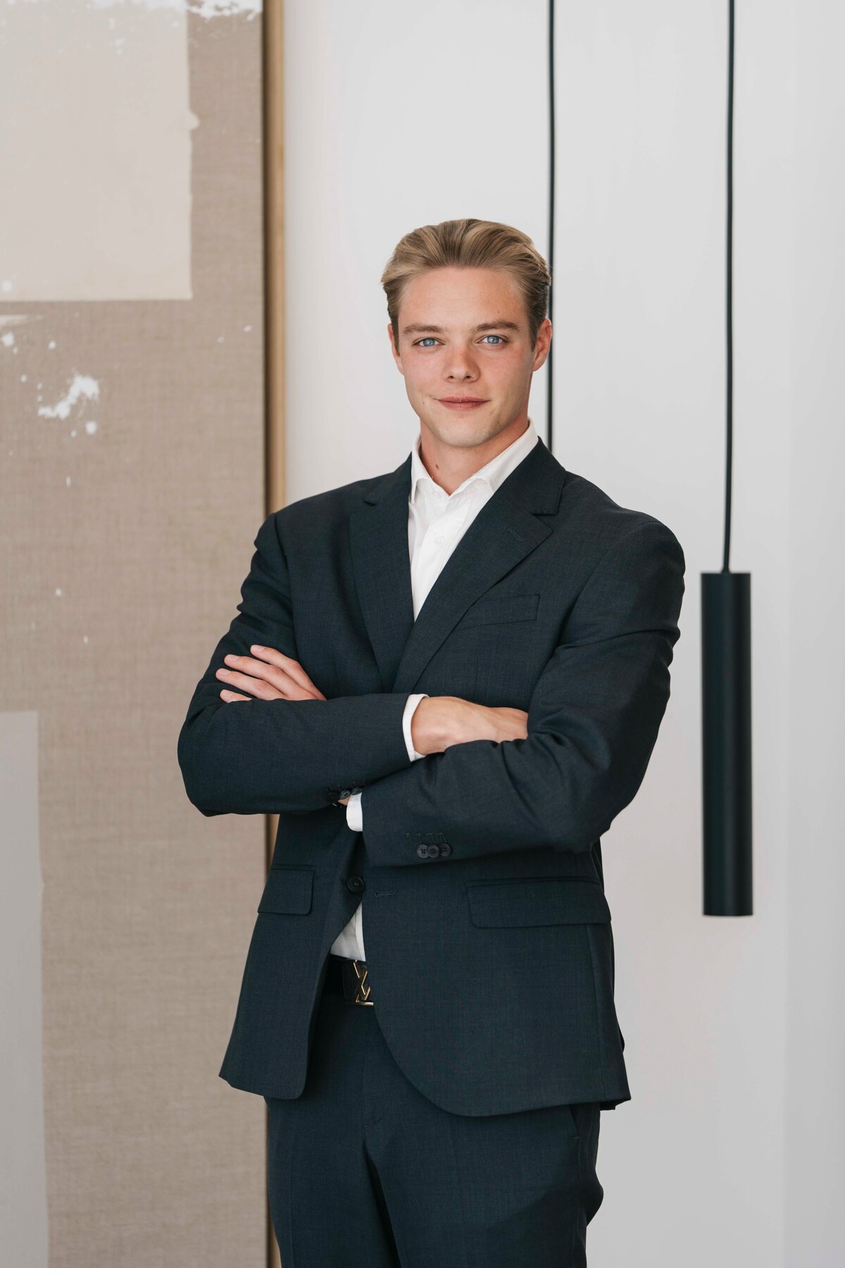 Rens Depraetere. Young man with blond hair, blue eyes, and fair skin, wearing a dark suit and posing confidently in a modern interior.