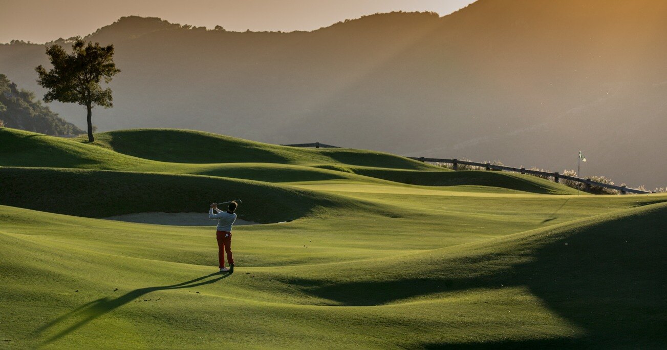 Golfer in La Zagaleta golf course in Benahavis, surrounded by rolling hills, with golden sunlight casting long shadows.