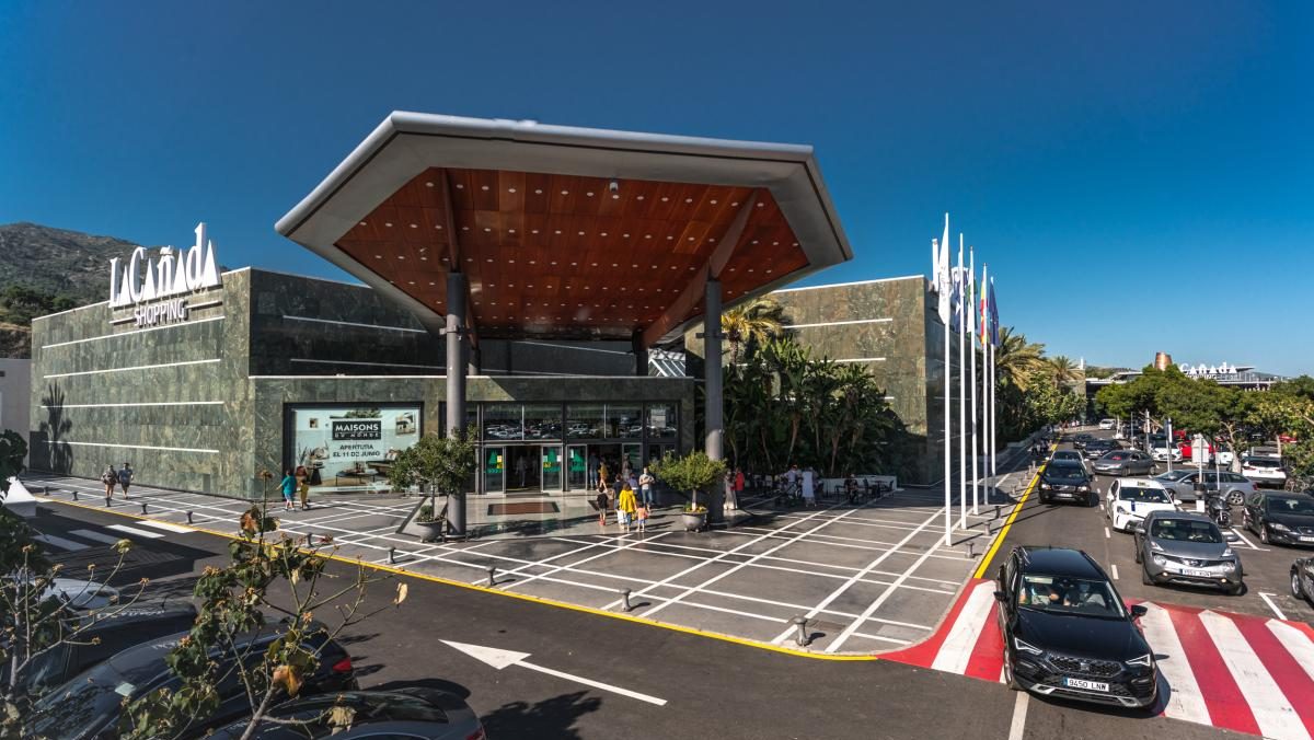 Entrance of La Cañada Shopping Centre in Marbella, featuring a modern canopy, glass facade, and a busy parking area