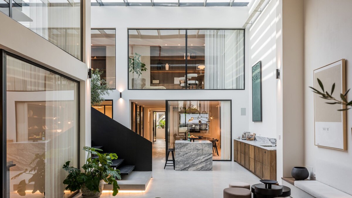 Norma Franck office in Marbella, featuring a modern double-height interior with floor-to-ceiling windows, sleek black staircase, and elegant natural finishes.