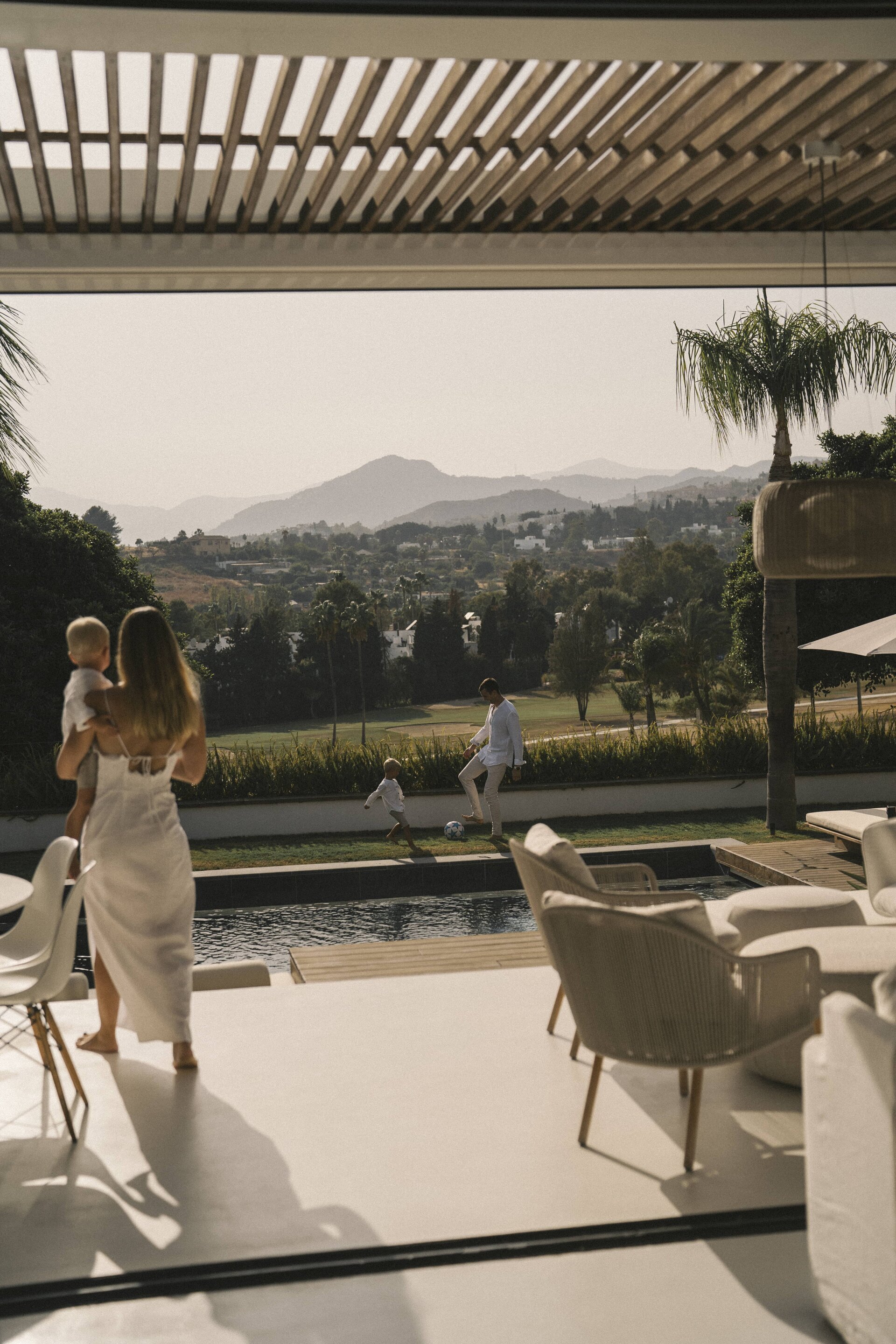 A family enjoying an outdoor terrace with a pool, overlooking a golf course and mountain views at sunset.