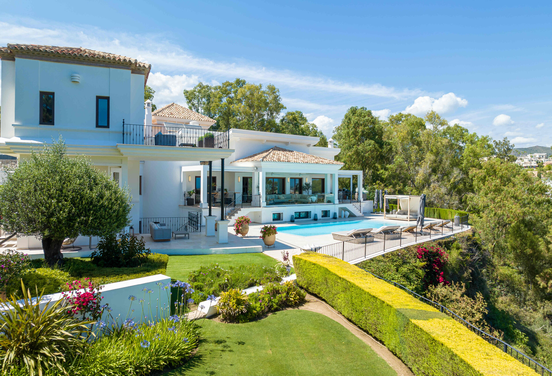 Elegant white villa in Marbella with a landscaped garden, infinity pool, and spacious terraces overlooking lush greenery.