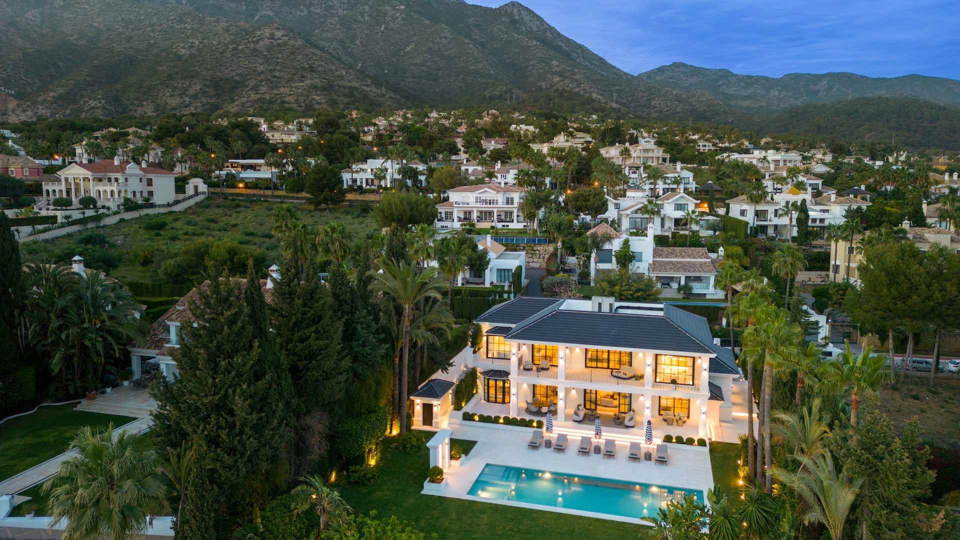 Aerial view of a villa in Sierra Blanca at dusk, surrounded by lush greenery and framed by a mountain.