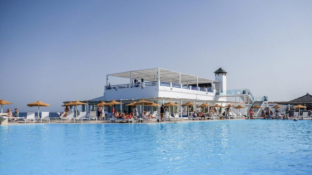 A vast light blue swimming pool with a white building behind.