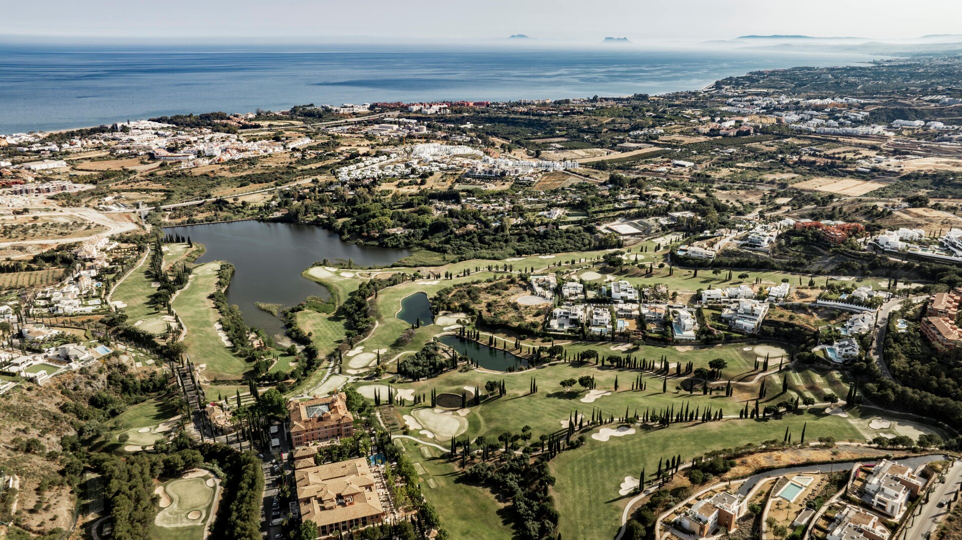 Aerial view of Villa Padierna and its golf courses, with lush greenery, lakes, and the Mediterranean Sea in the background.