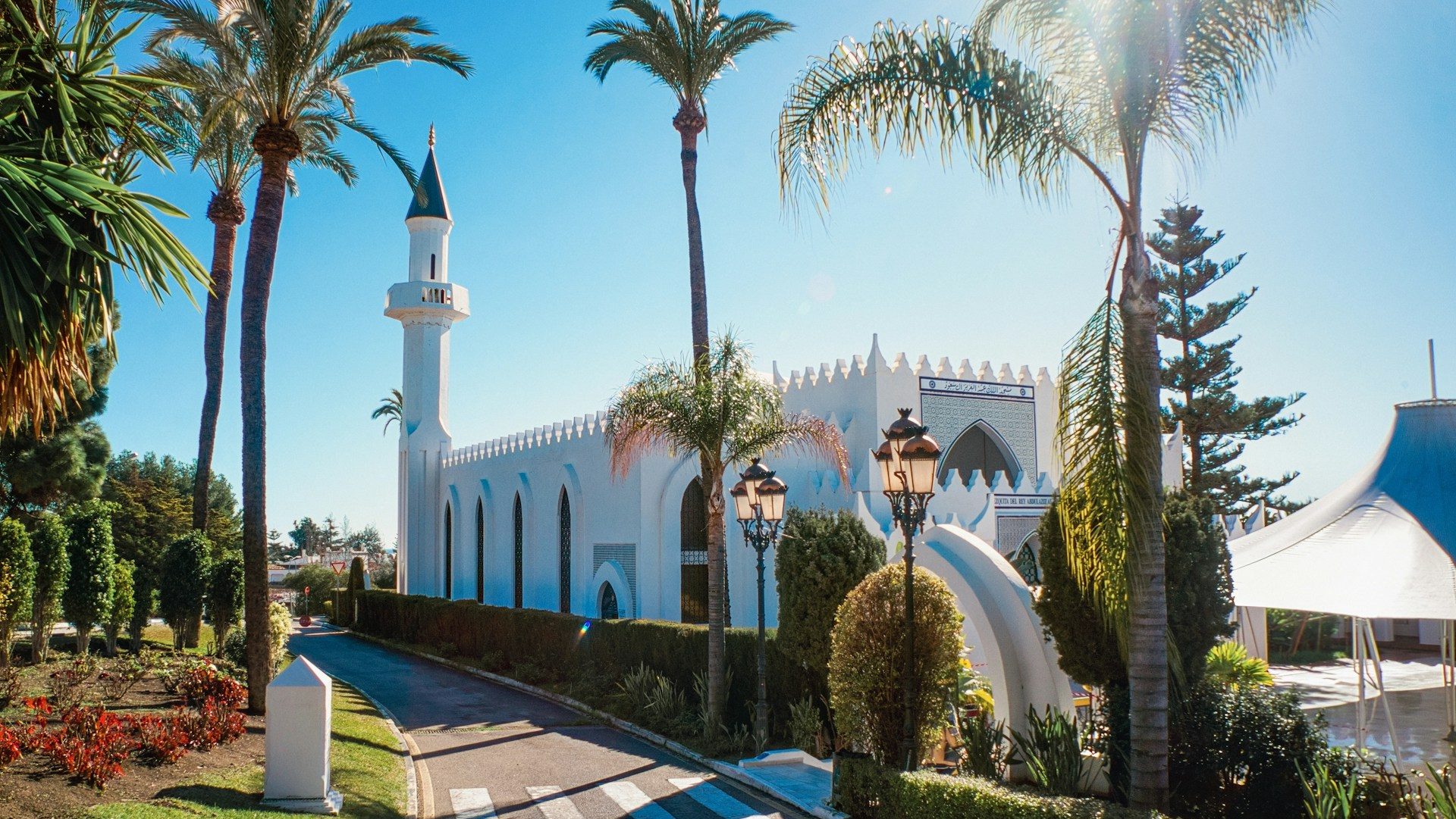 The Marbella Grand Mosque, with its distinctive white Moorish architecture, featuring a tall minaret and beautifully landscaped surroundings with palm trees and decorative lamp posts.