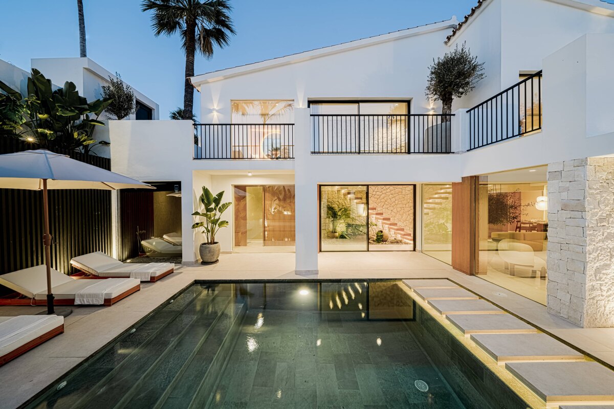 Villa Botán. Modern Mediterranean villa with white façades, black accents, an illuminated pool, and open terraces surrounded by lush greenery.