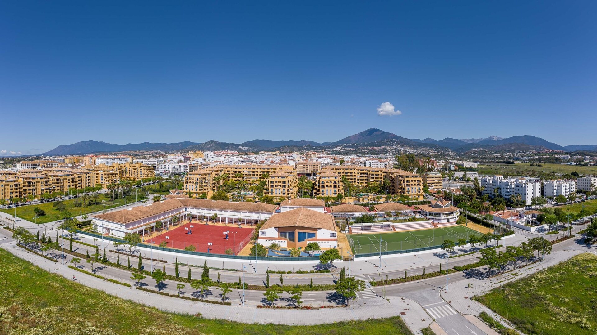 Aerial view of Laude school in San Pedro Alcántara, featuring sports courts, green spaces, and terracotta-roofed buildings.