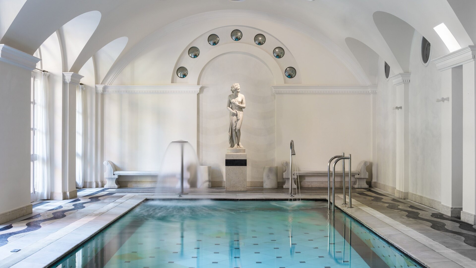 Elegant indoor spa at Villa Padierna, featuring a classical statue, arched ceilings, and a heated pool with cascading water jets.