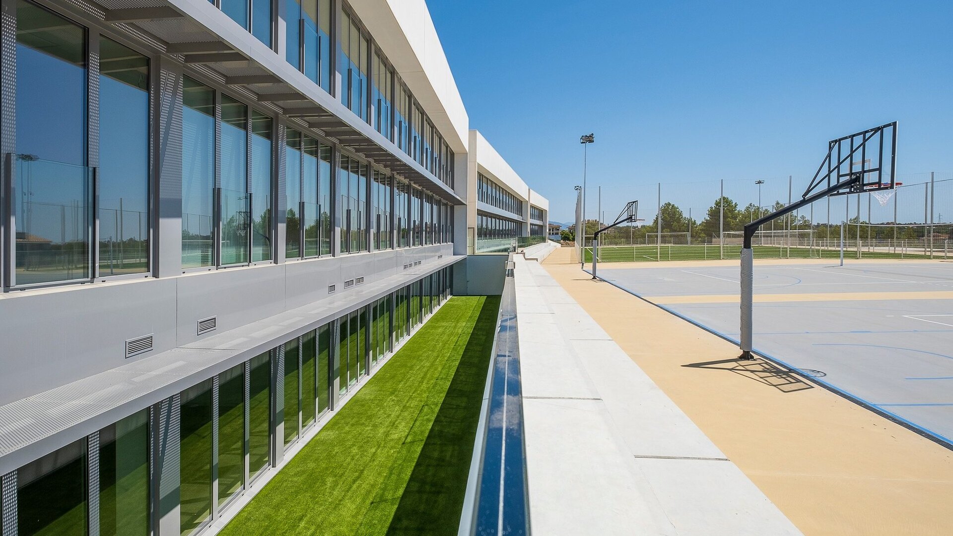 Atlas American School in Estepona, featuring a modern glass facade and outdoor basketball courts under a clear blue sky.