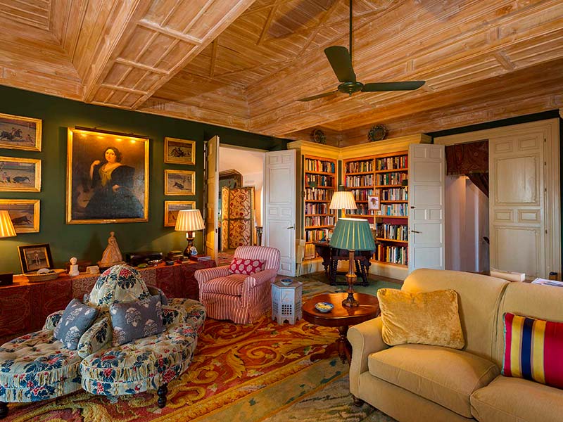 Classic living room in Alcuzcuz, Benahavís, featuring wooden ceilings, antique furniture, a library, and warm lighting.