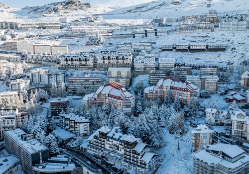 Aerial view of Sierra Nevada covered in snow, featuring alpine-style buildings, ski resorts, and mountain slopes.