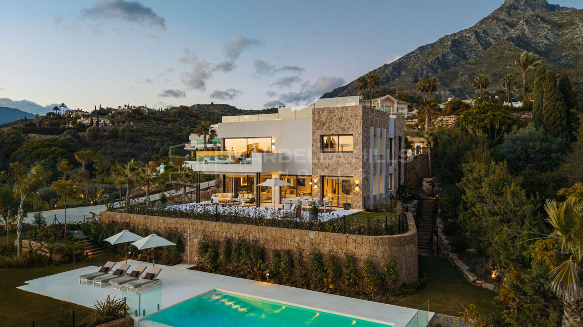 Contemporary villa in Marbella Hill Club at dusk, with the Sierra Blanca mountains behind