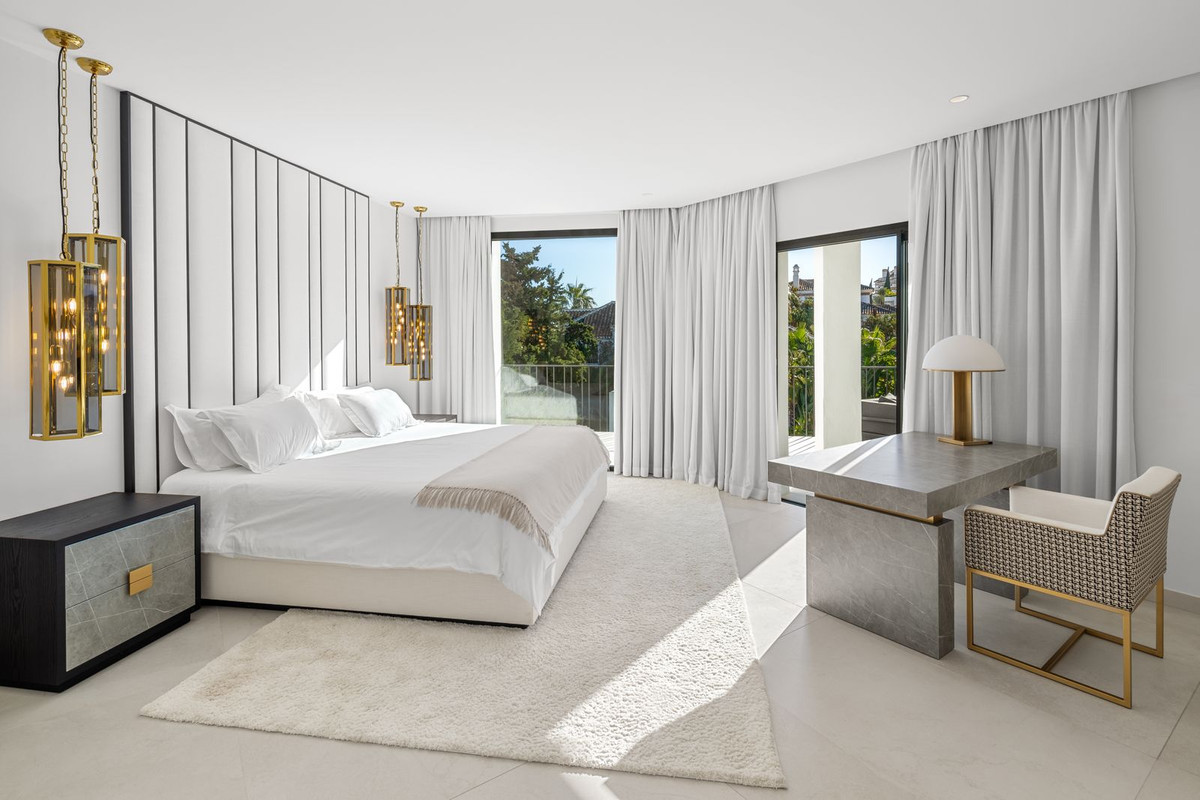 Bright bedroom with a large bed, two chandeliers, a desk, and floor-to-ceiling windows.