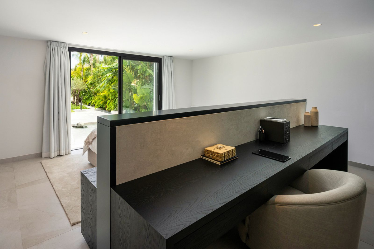 Bedroom with a dark wooden desk and partition, facing large sliding glass doors to a lush garden.