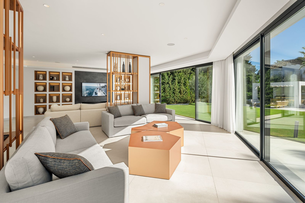 Spacious living room with light gray sofas, modern coffee tables, and large glass doors opening to a lawn.