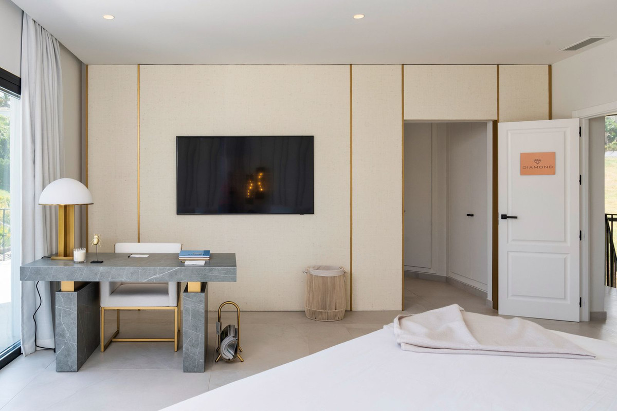 Bedroom featuring a gray desk, white chair, wall-mounted television, and a doorway leading to another room.