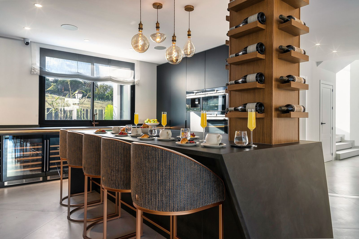 Modern kitchen island with breakfast setting, wine rack, and large window overlooking greenery.
