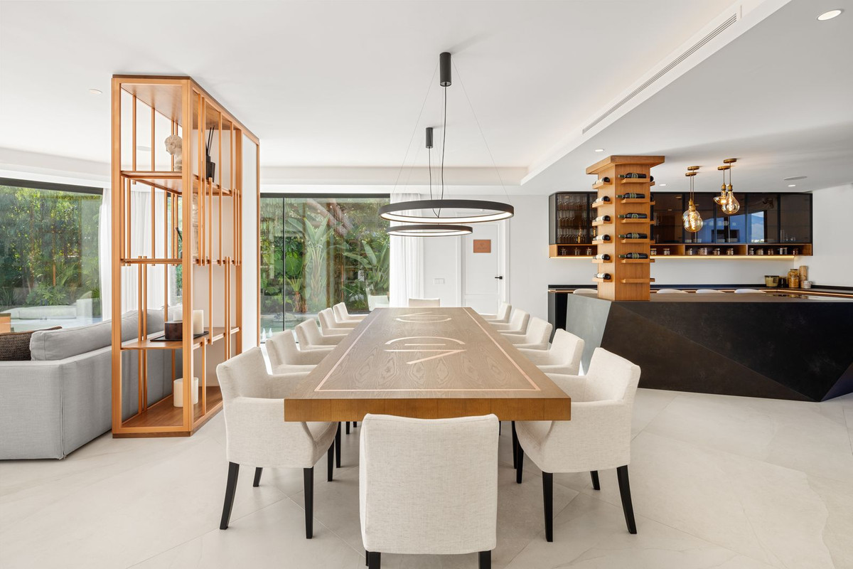 Dining room features a long wooden table, twelve chairs, and a contemporary chandelier. Wine rack is visible.