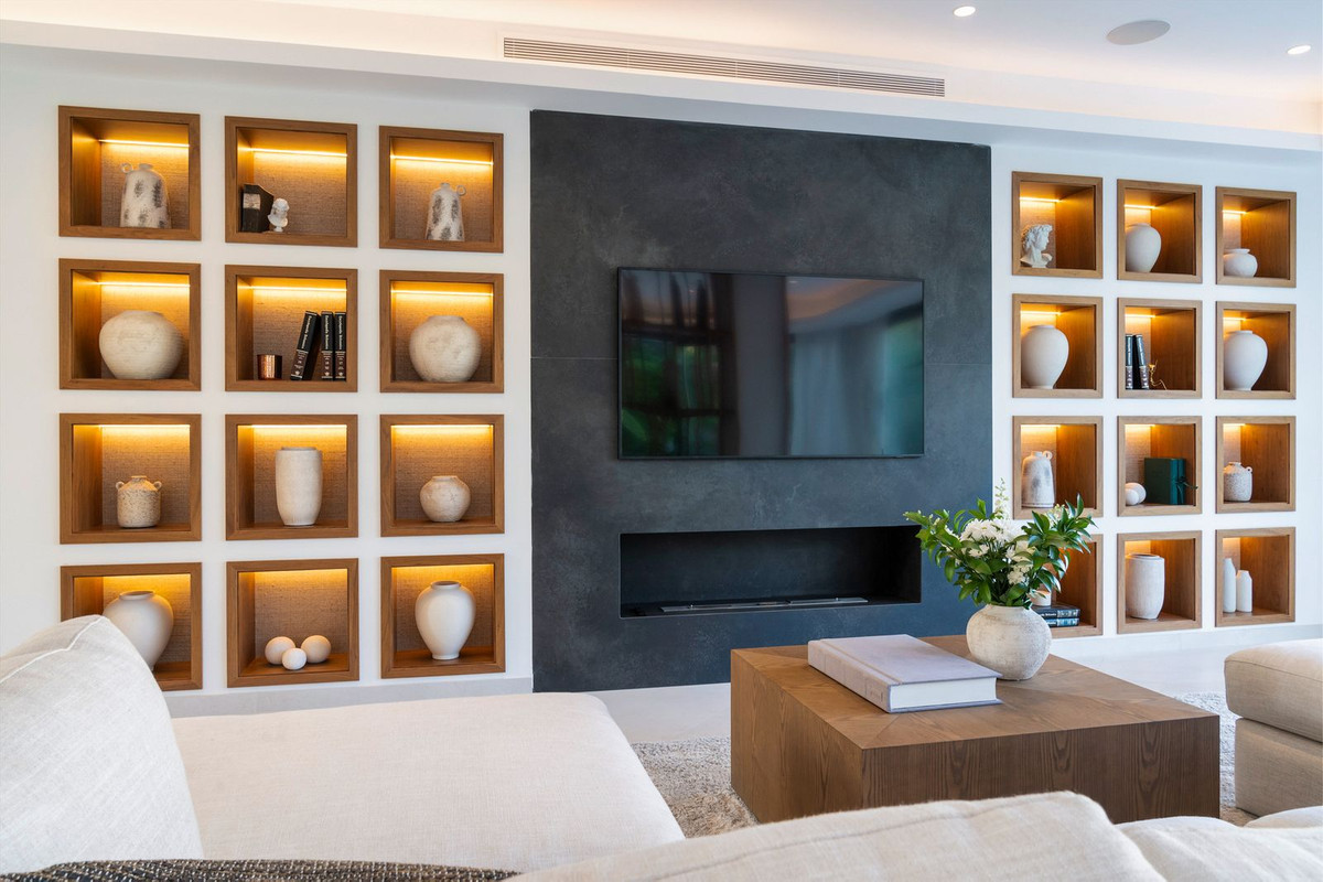 Living room with integrated TV, modern fireplace, and illuminated shelving displaying decorative vases.