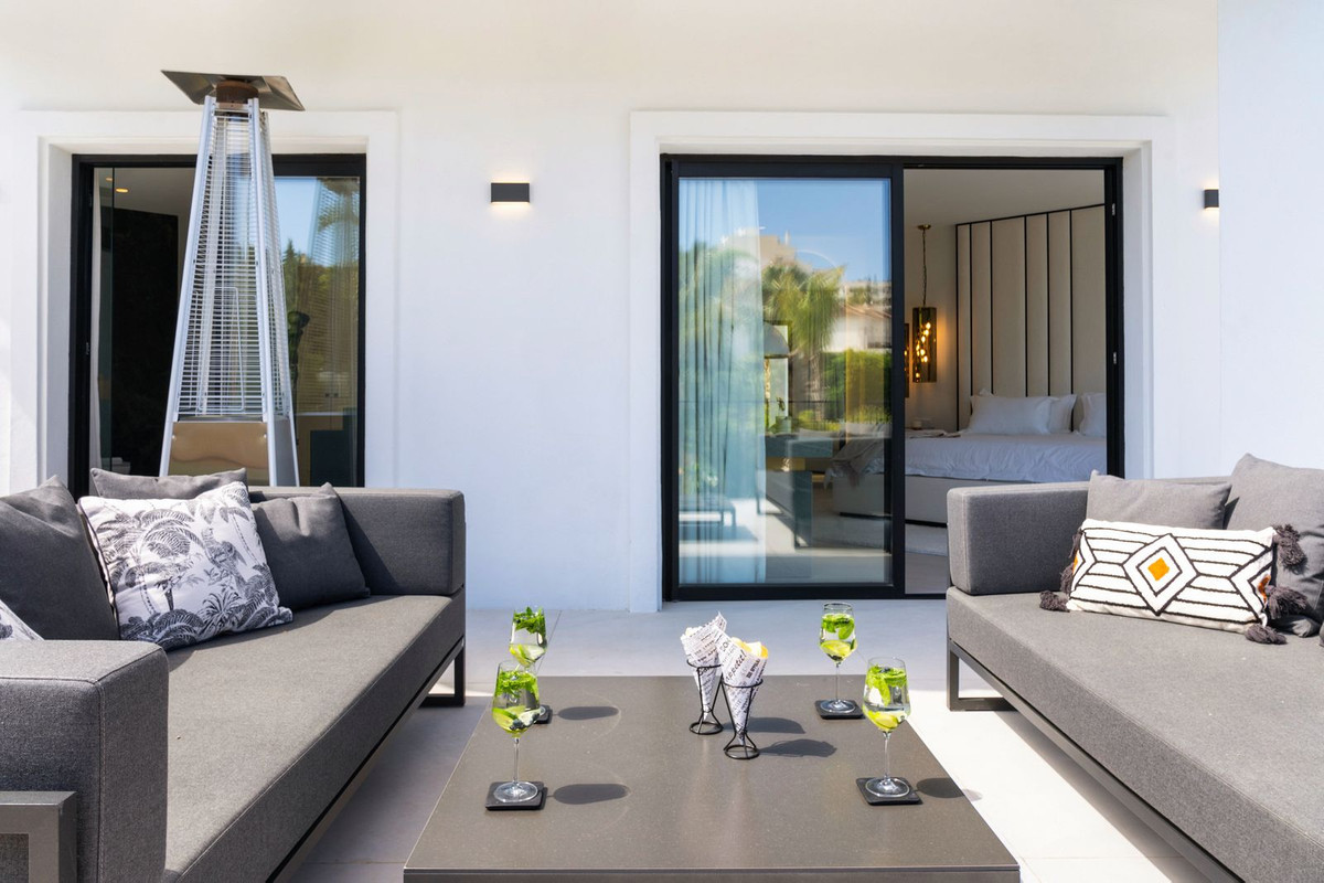 Outdoor patio with two gray sofas, a coffee table with drinks, and a visible bedroom through a glass door.
