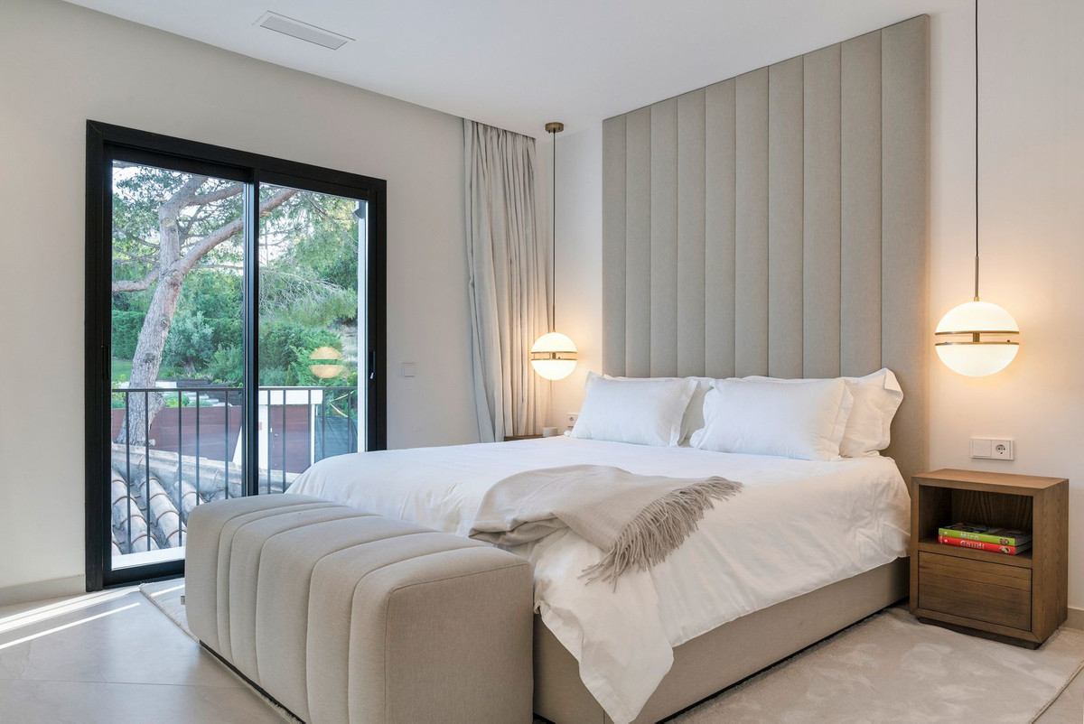 Bedroom with large bed, upholstered headboard, hanging lights, and glass doors to a balcony.