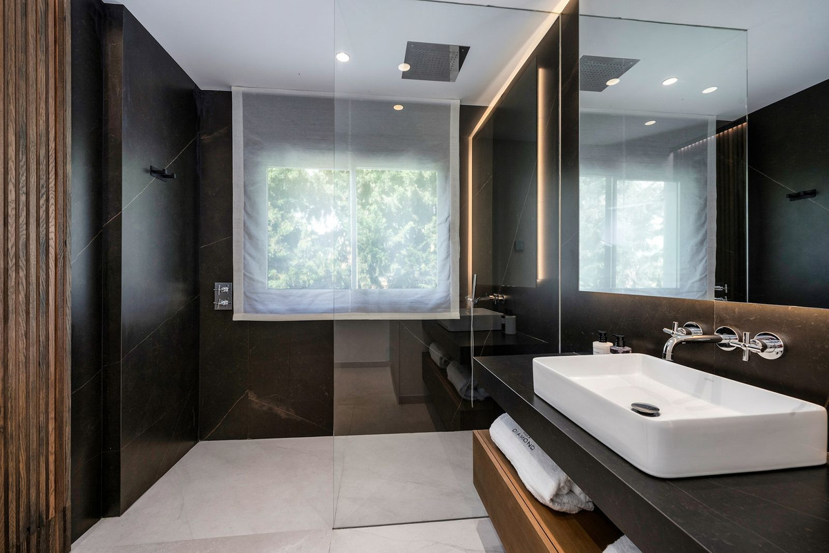Modern bathroom with dark tiled walls, glass shower, black vanity, and rectangular sink.