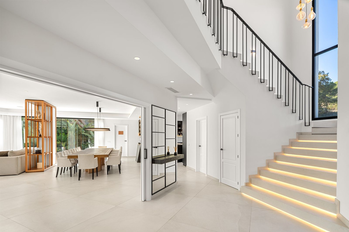 White-walled entrance hall with an illuminated staircase leading upstairs and a dining room visible beyond.