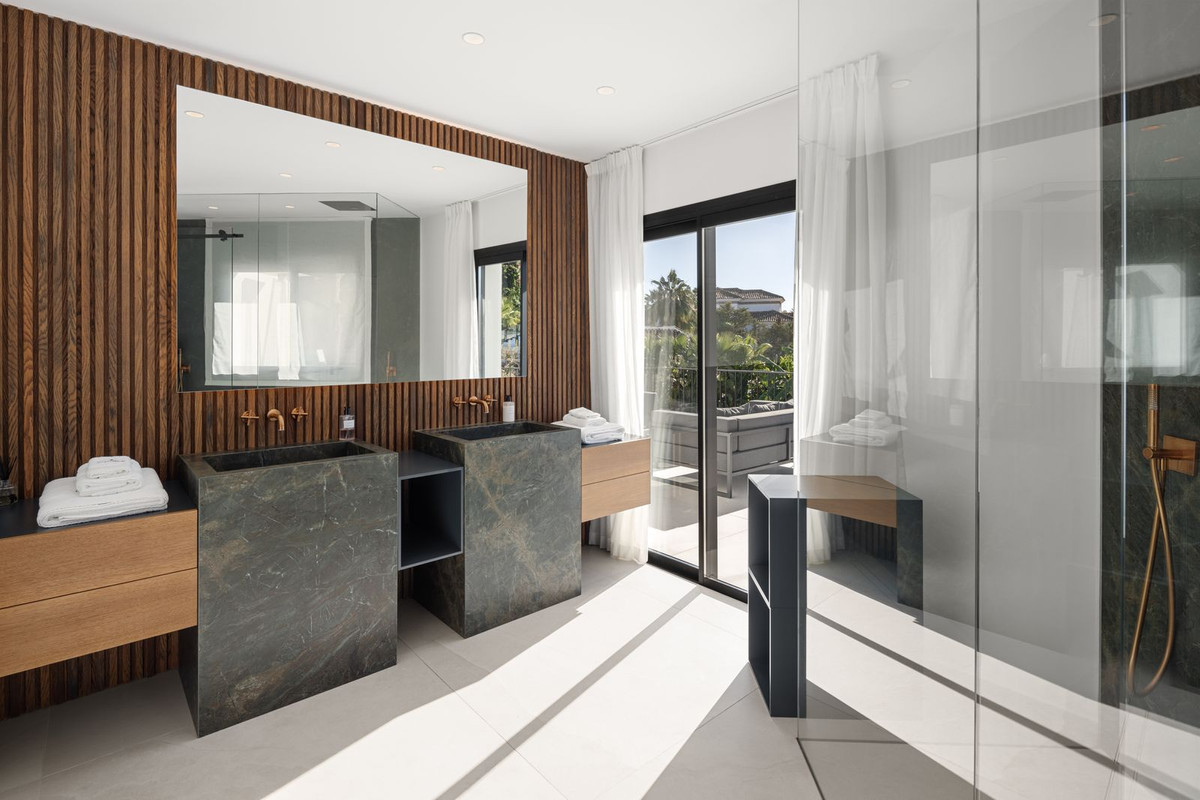 Modern bathroom with two stone sinks, large mirror, wooden slatted wall, and sliding glass doors to a balcony.